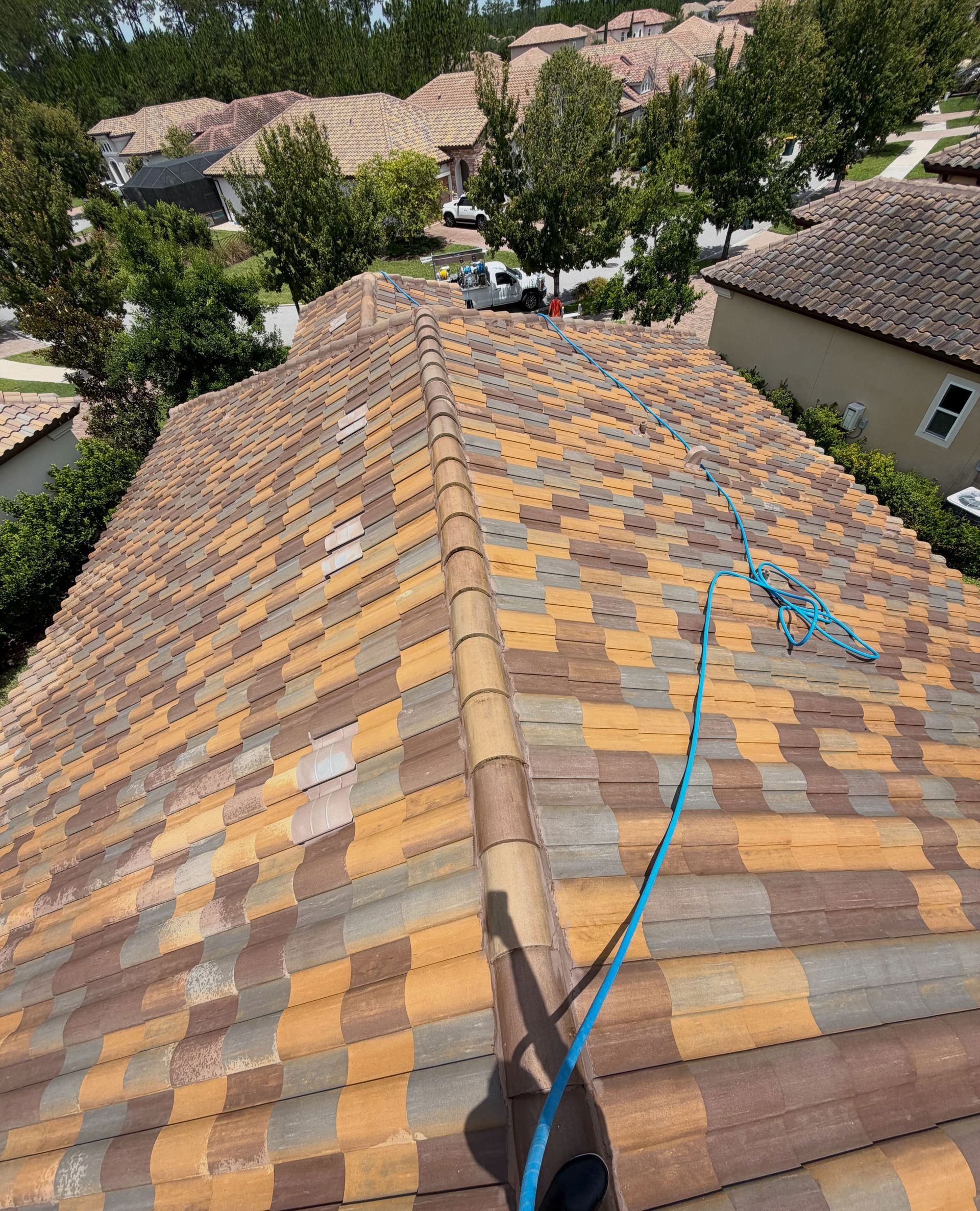 Roof with multicolored tiles under repair, blue hose on the ridge, seen from above