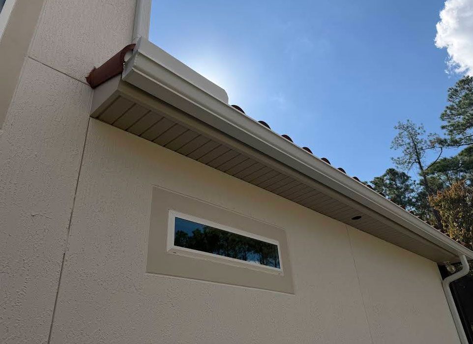 Exterior of a beige house with a white roof eave and narrow window under a blue sky