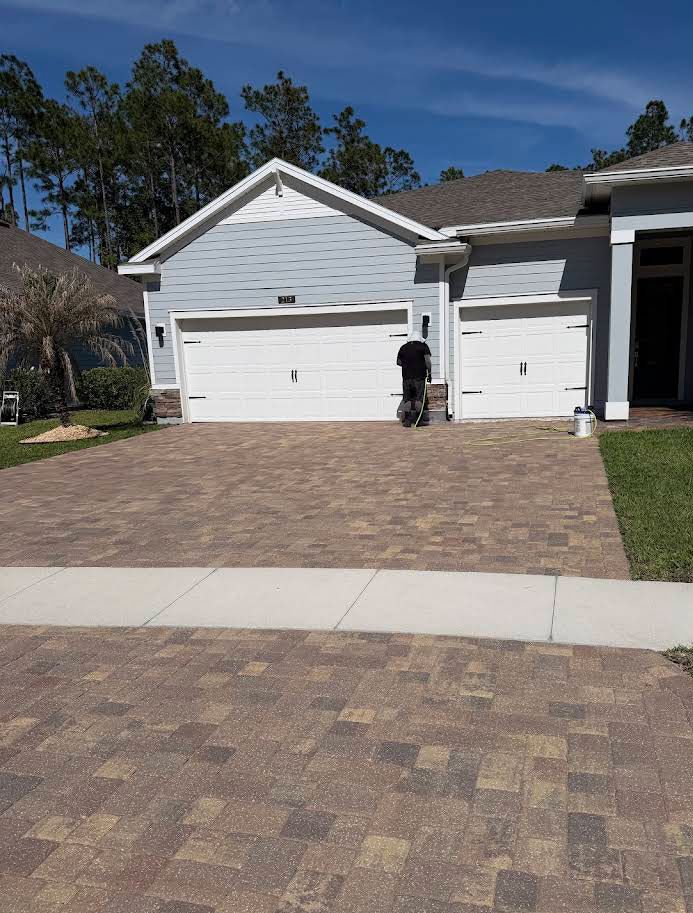 Suburban house with white garage doors and a brick driveway; a person stands near the garage.