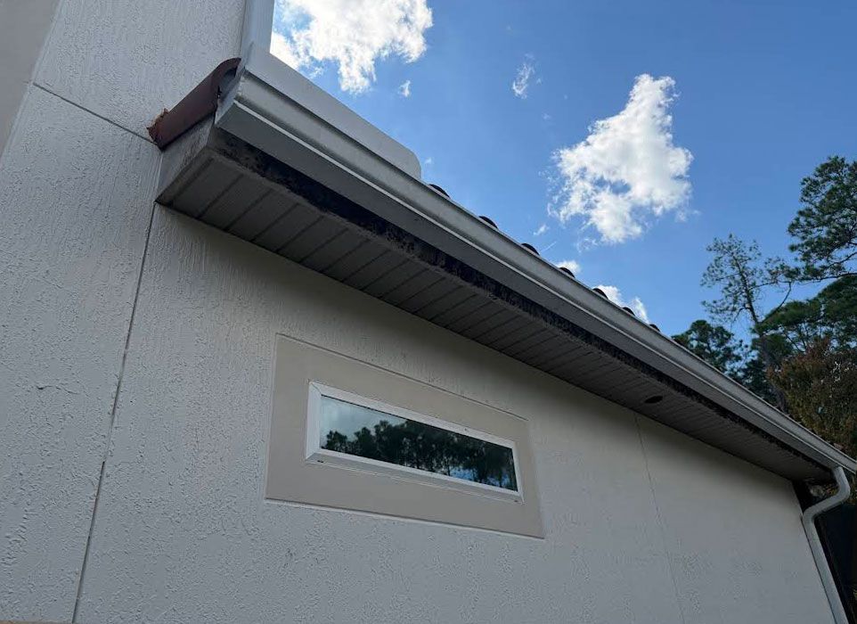 White house exterior with a slanted roof and a narrow horizontal window under a blue sky.