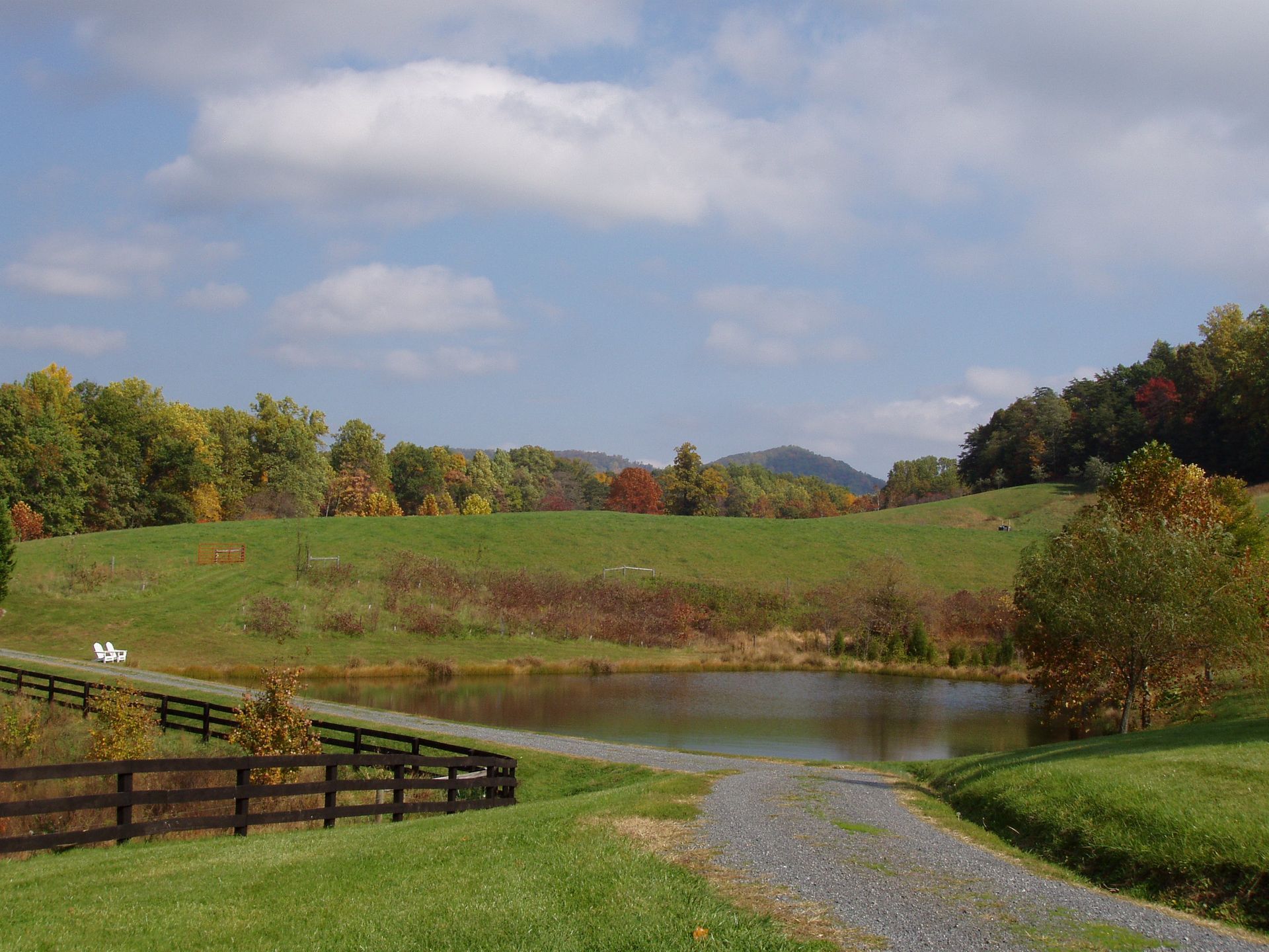 A dirt road leads to a pond in the middle of a grassy field