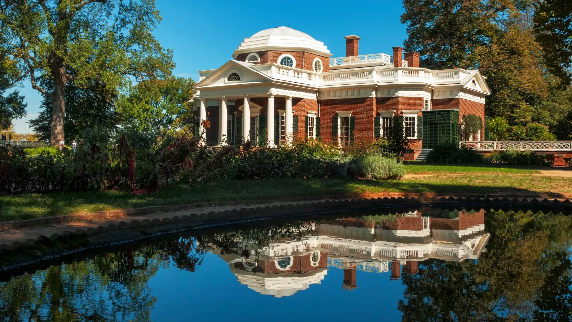 A large brick house is reflected in a pond.