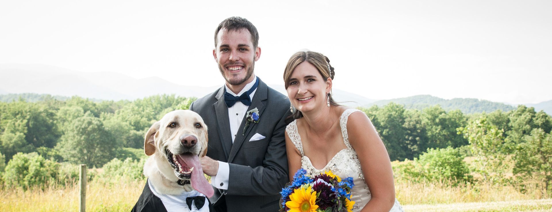 A bride and groom are posing for a picture with their dog.