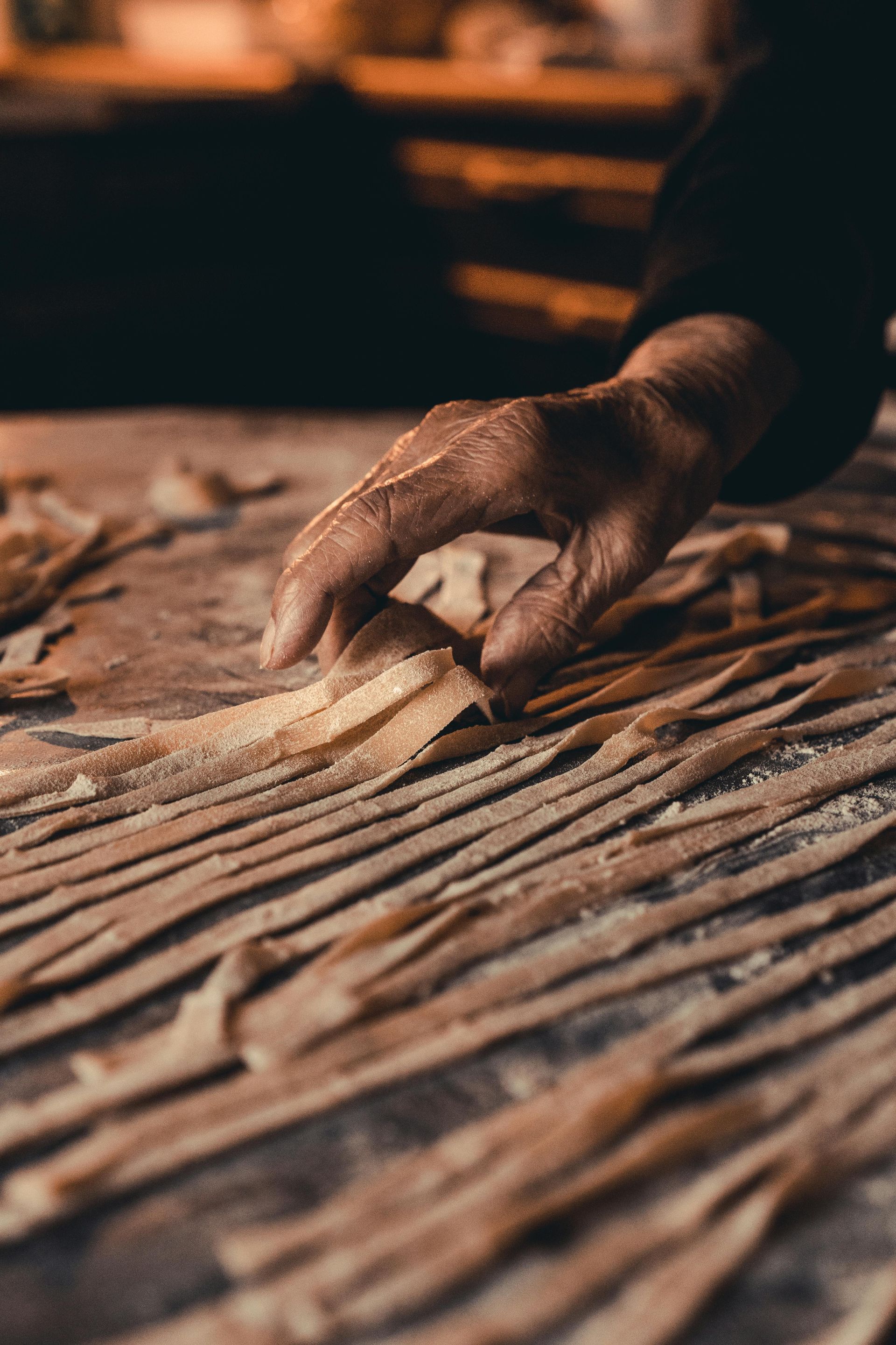 Hand arranging fresh pasta strands on a wooden surface.