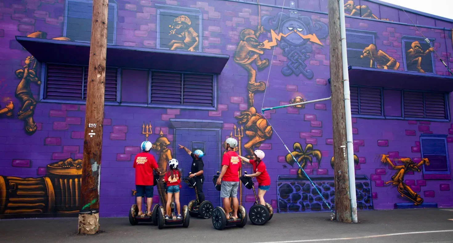 Five people with Segways pose in front of a purple mural-covered building.