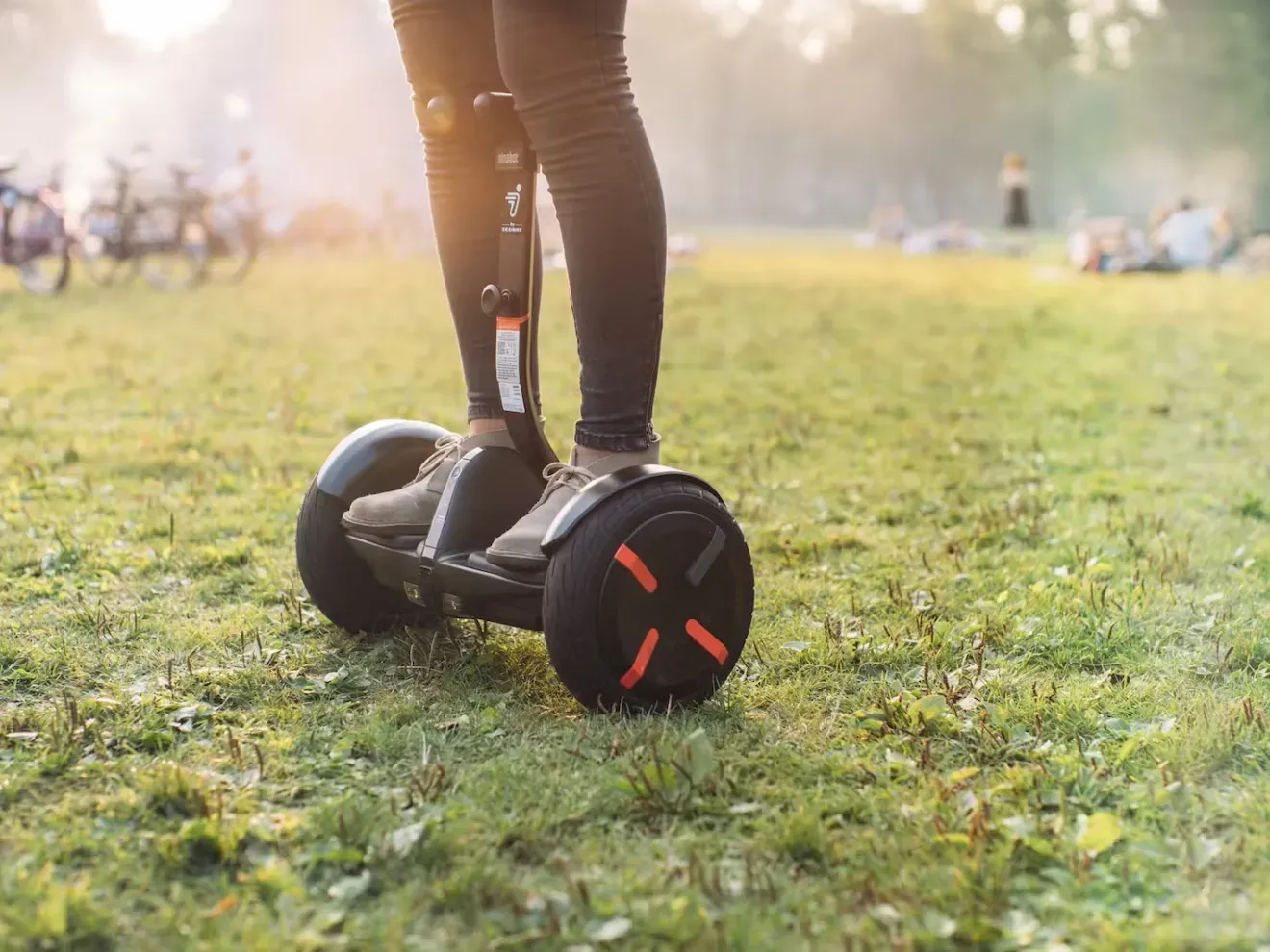 Person riding a black hoverboard on grass in a sunlit park