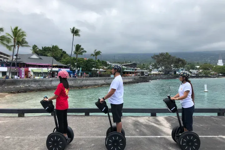 Three people ride Segways along a seaside promenade under cloudy skies.