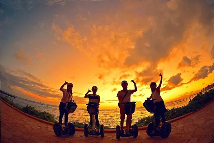 Four people on electric scooters silhouetted against a vivid orange sunset outdoors
