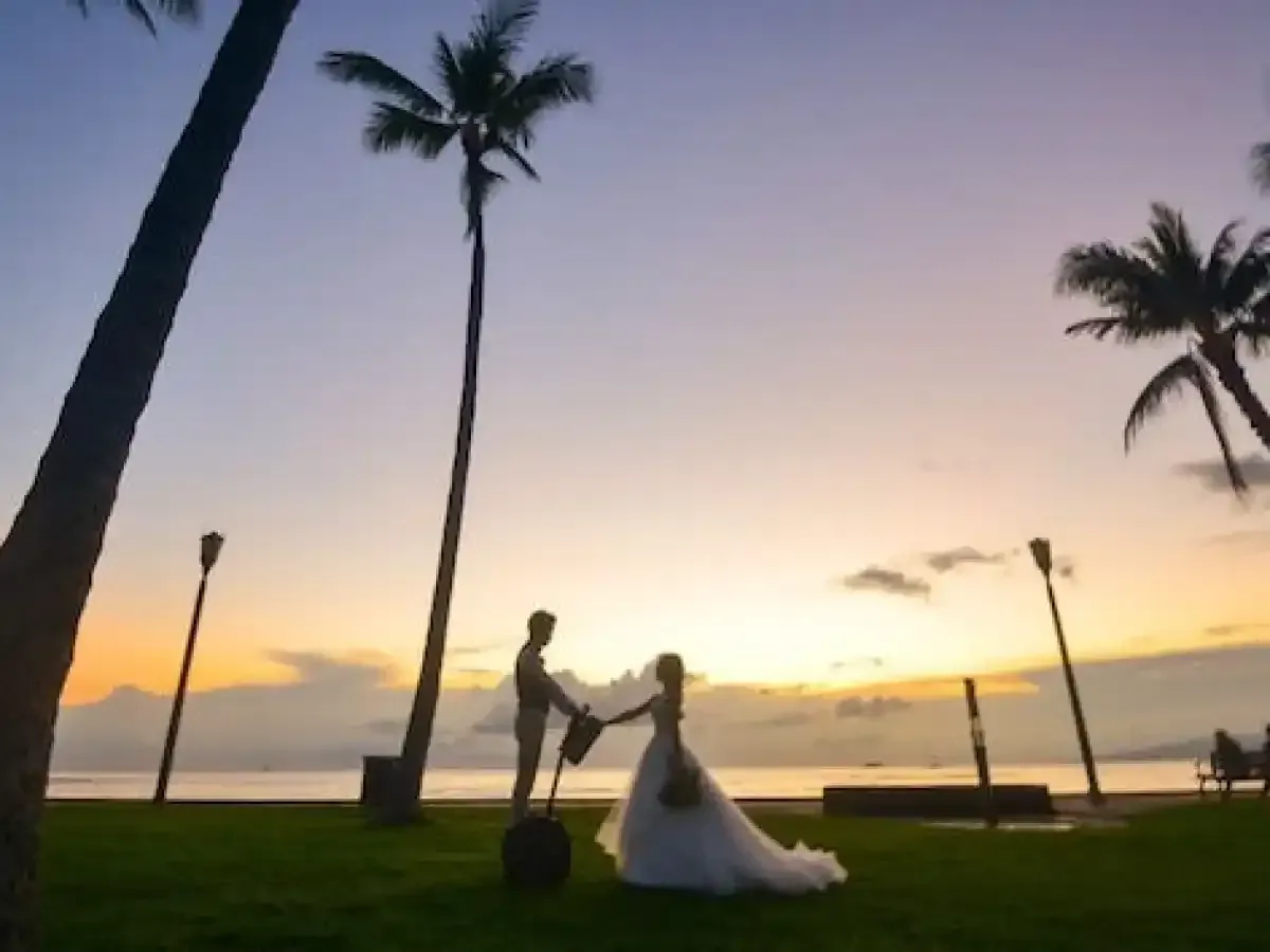 Silhouetted couple at sunset on a beach, with palm trees and the bride holding hands with the groom