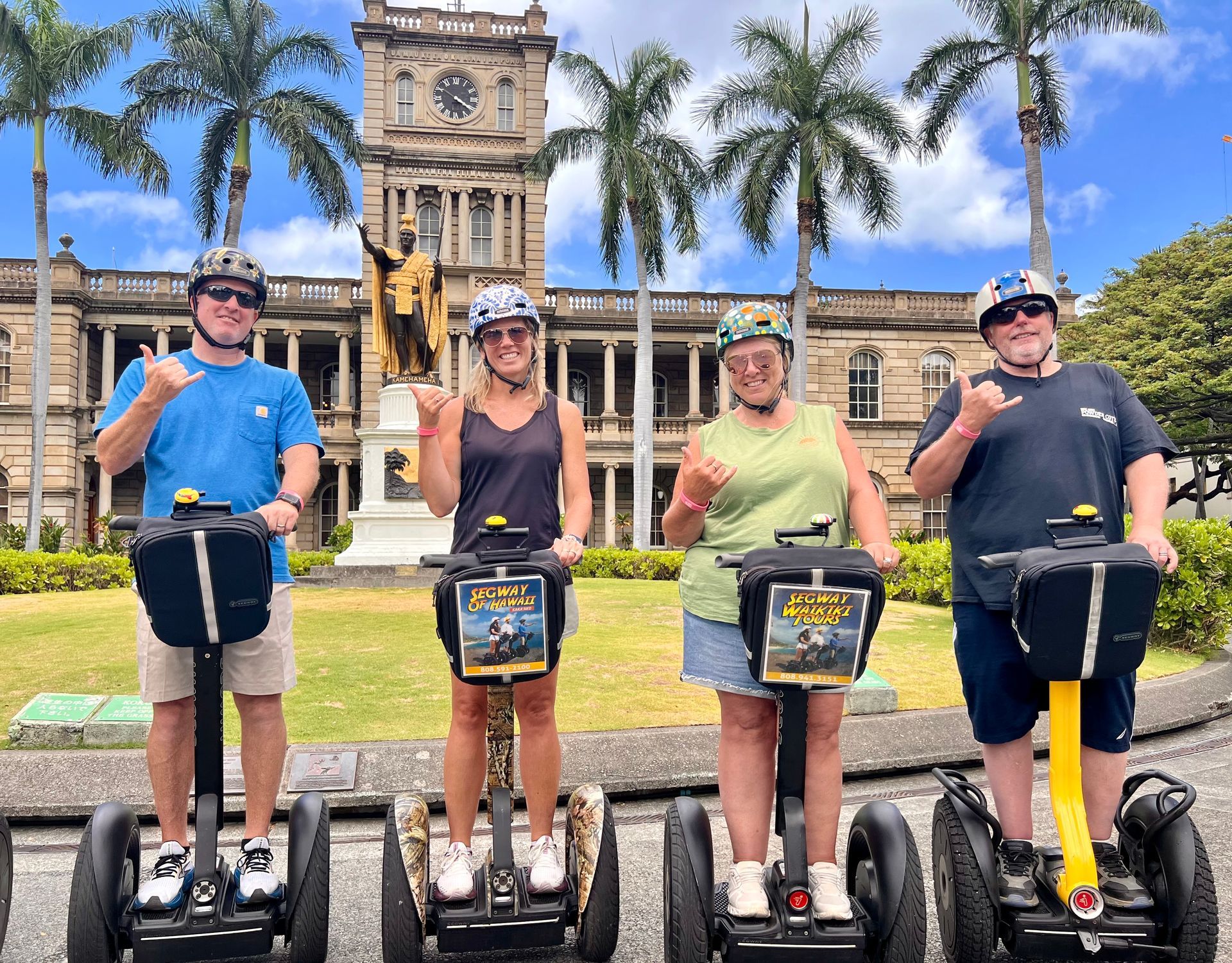 Four people riding Segways in front of a historic building with palm trees and a blue sky