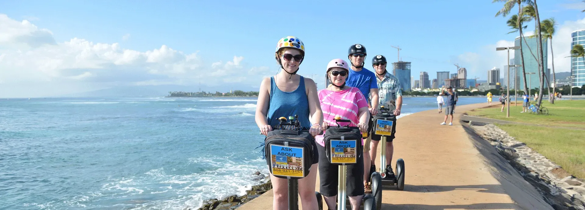 Cyclists riding along a sunny seaside path beside the ocean and palm trees