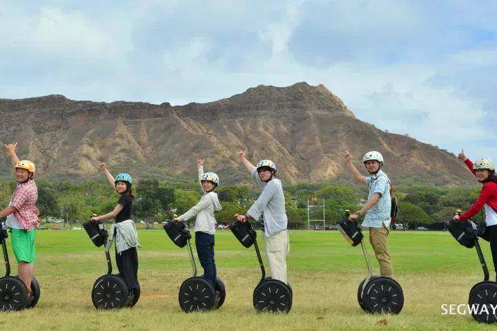 People riding Segways in a grassy field with rocky hills and blue sky in the background