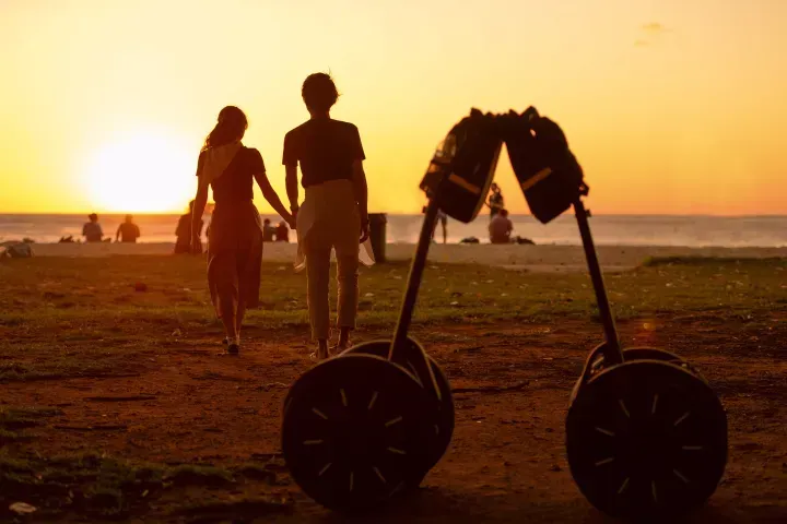 Silhouetted couple walking on a beach at sunset beside a large stroller-like frame