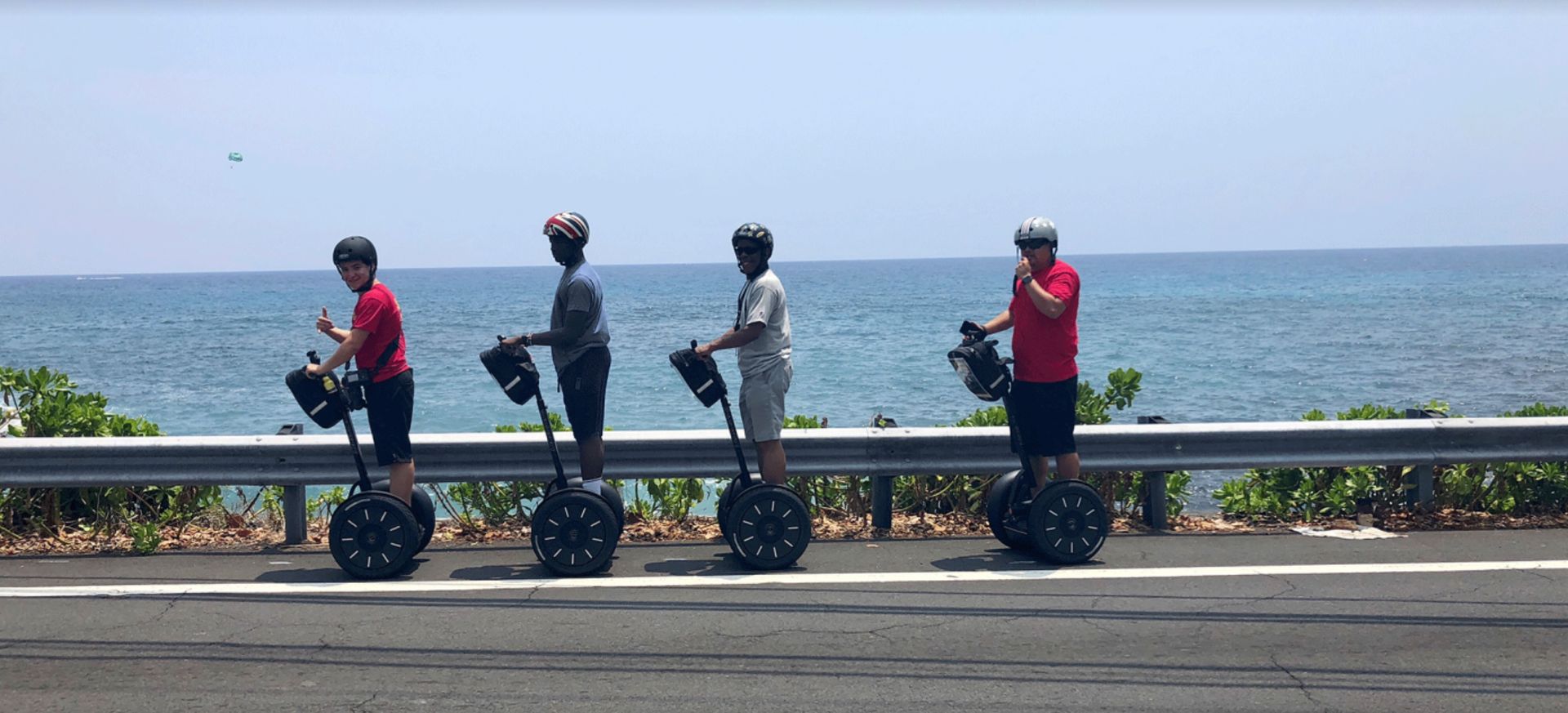 Four people on Segways along a seaside road, with ocean and railing in the background.