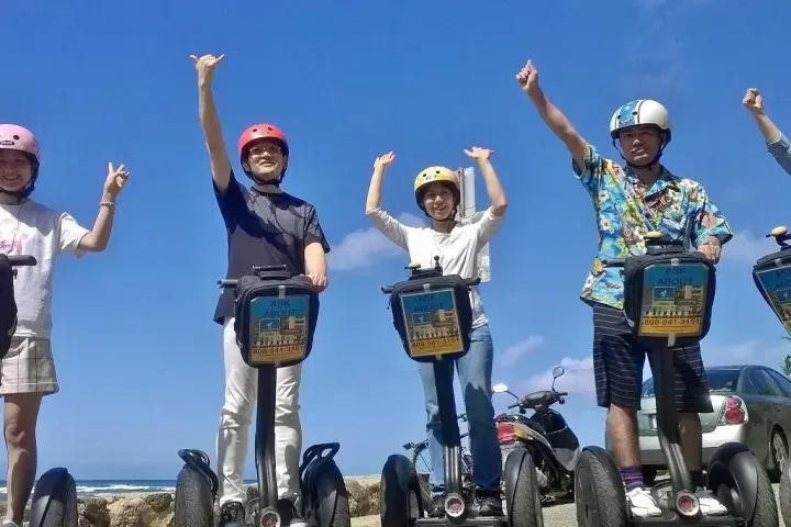 Four people on Segways raise their arms on a sunny outdoor road under a blue sky.