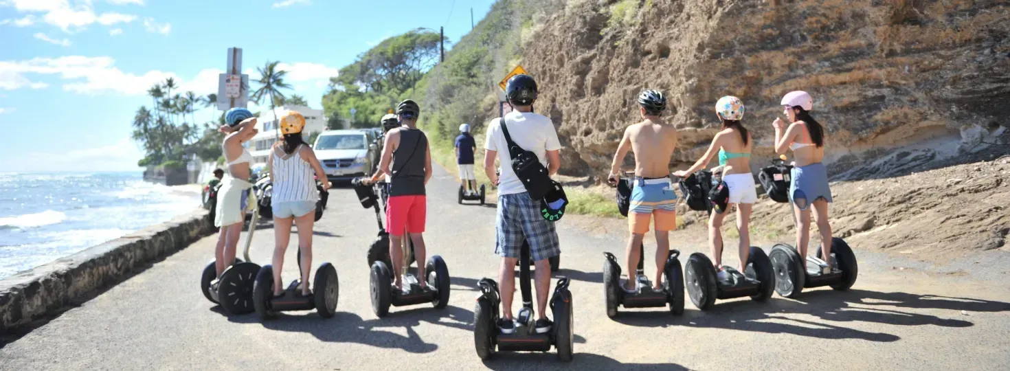 Group riding Segways on a sunny coastal path beside a cliff and ocean