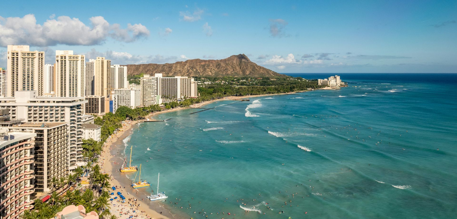 Aerial view of a tropical beachfront with high-rise hotels, turquoise water, and a long sandy shore