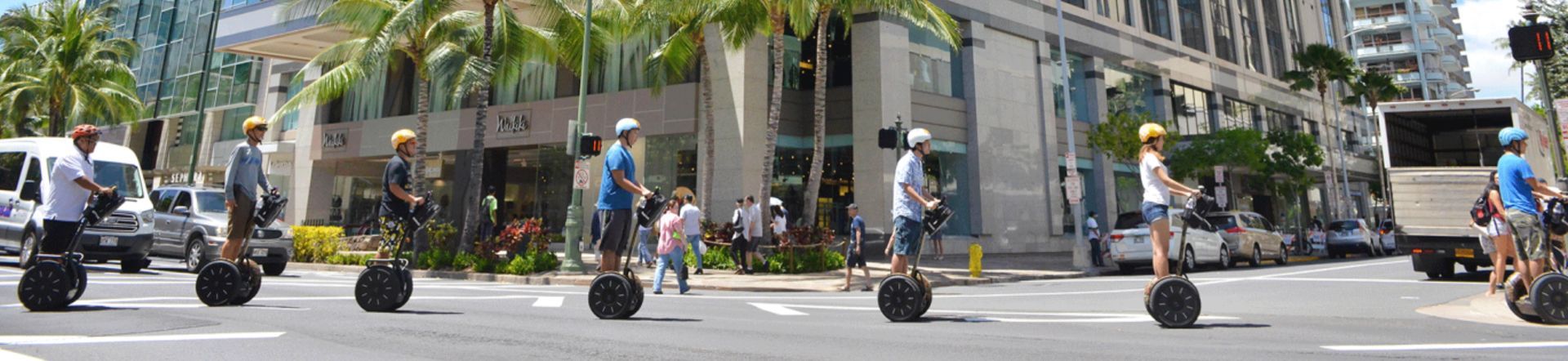 Pedestrians and cyclists crossing a palm-lined city street outside modern buildings