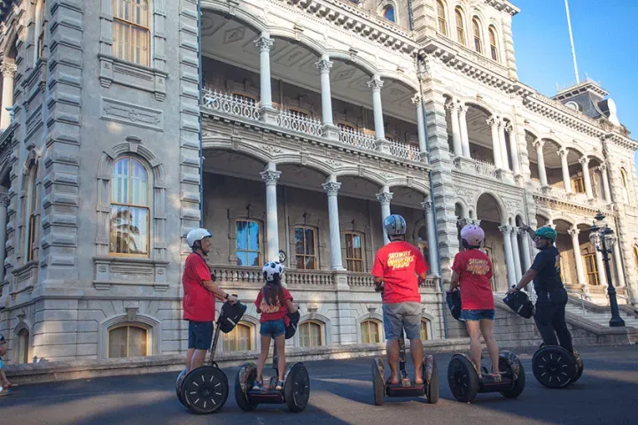 People riding Segways in front of a grand historic building with ornate balconies.