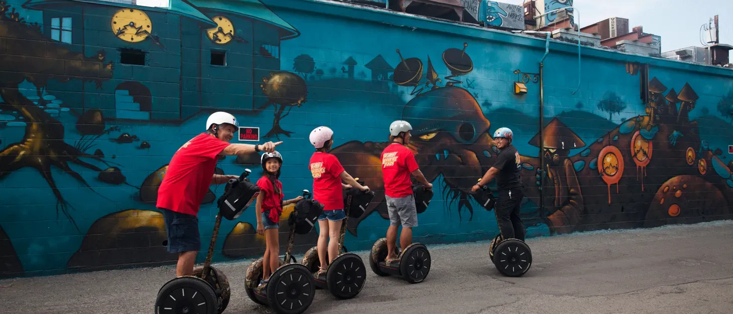 Five people in red shirts riding electric unicycles past a colorful ocean mural
