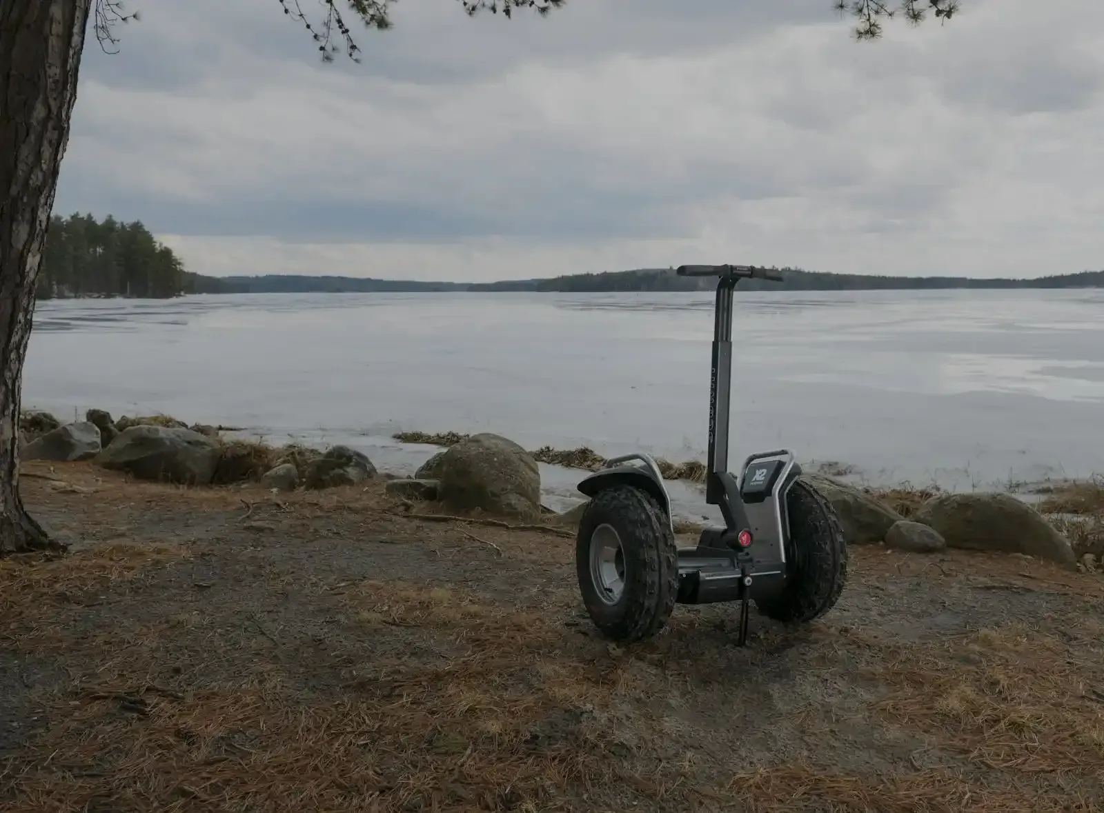 A small motorized scooter parked on a rocky shore overlooking a frozen lake under a cloudy sky.