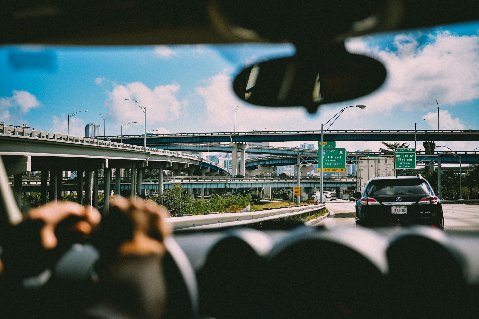 View from a car driving on a highway with overpasses and city buildings under a blue sky.