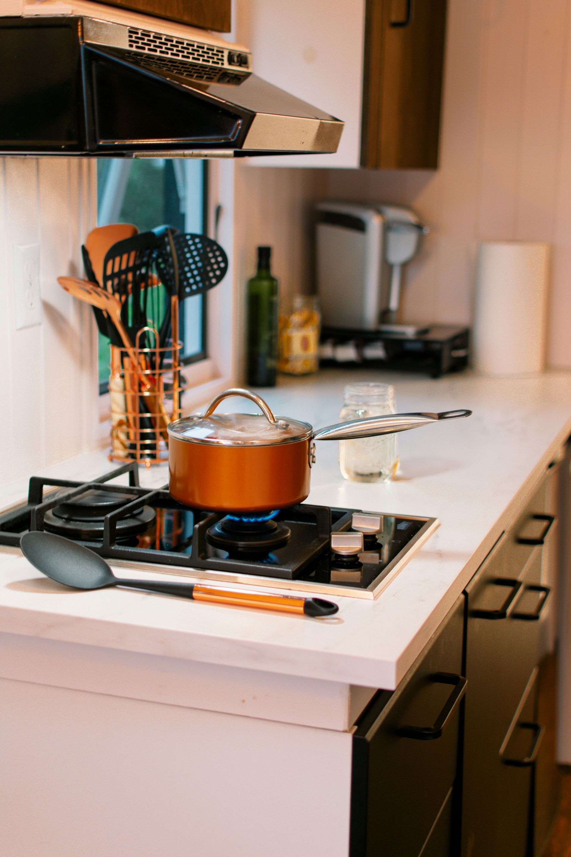 Copper pot on a stove burner in a kitchen, with utensils, window, and countertop.