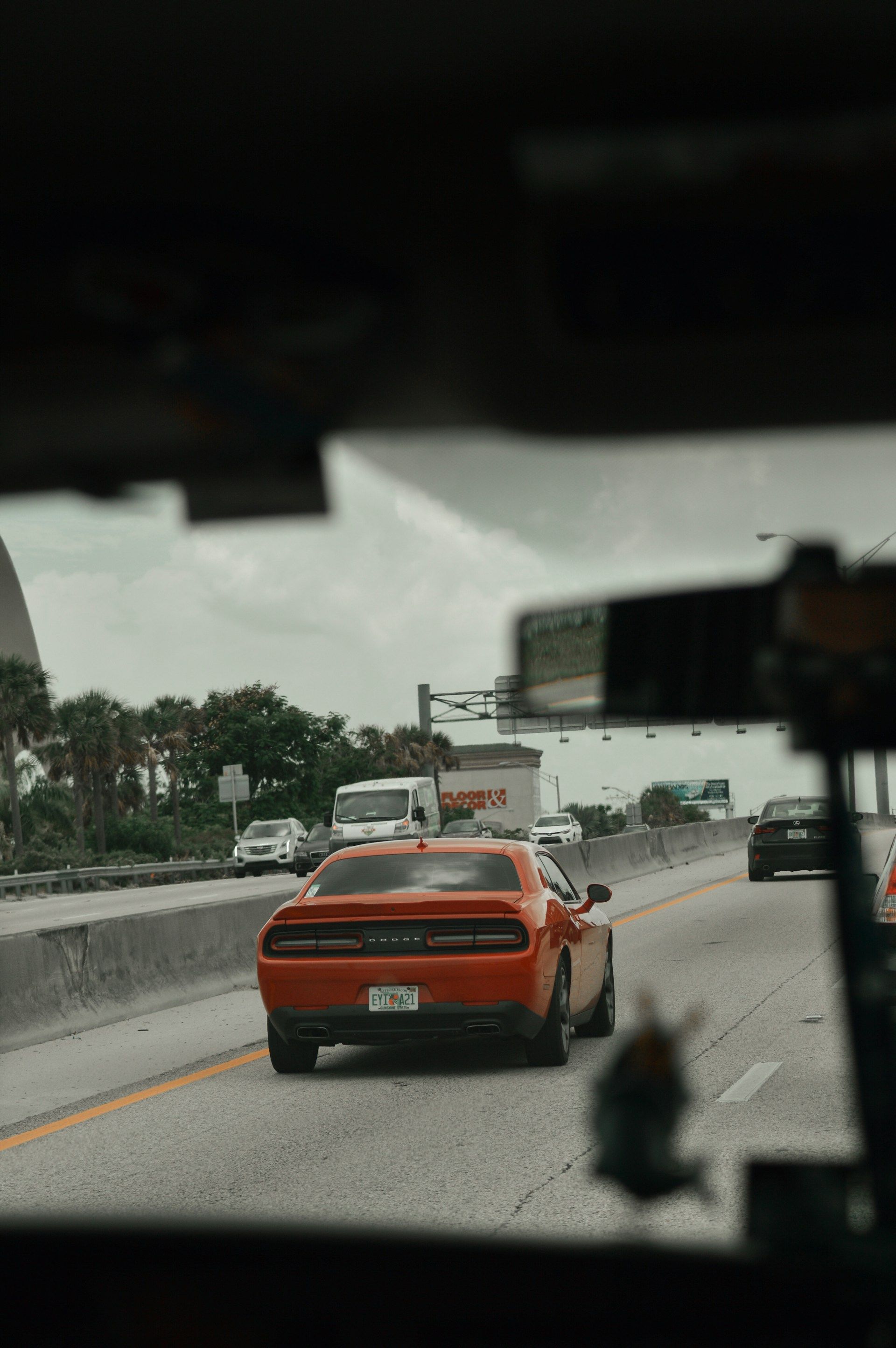 Orange Dodge Challenger car driving on a highway, viewed from inside another vehicle on an overcast day.