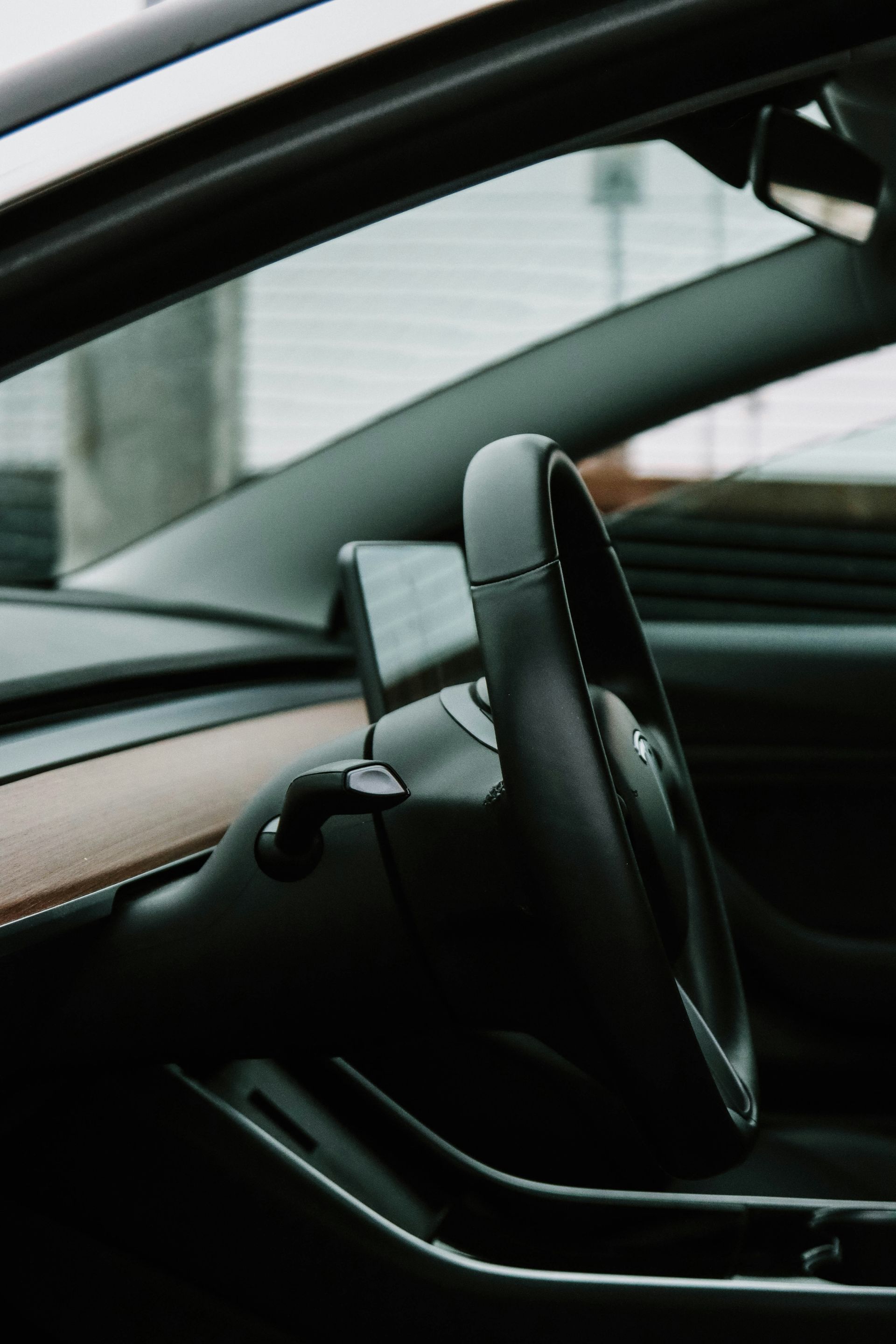 Interior of a Tesla car, focused on the black steering wheel and dashboard, with a glimpse of the outside.