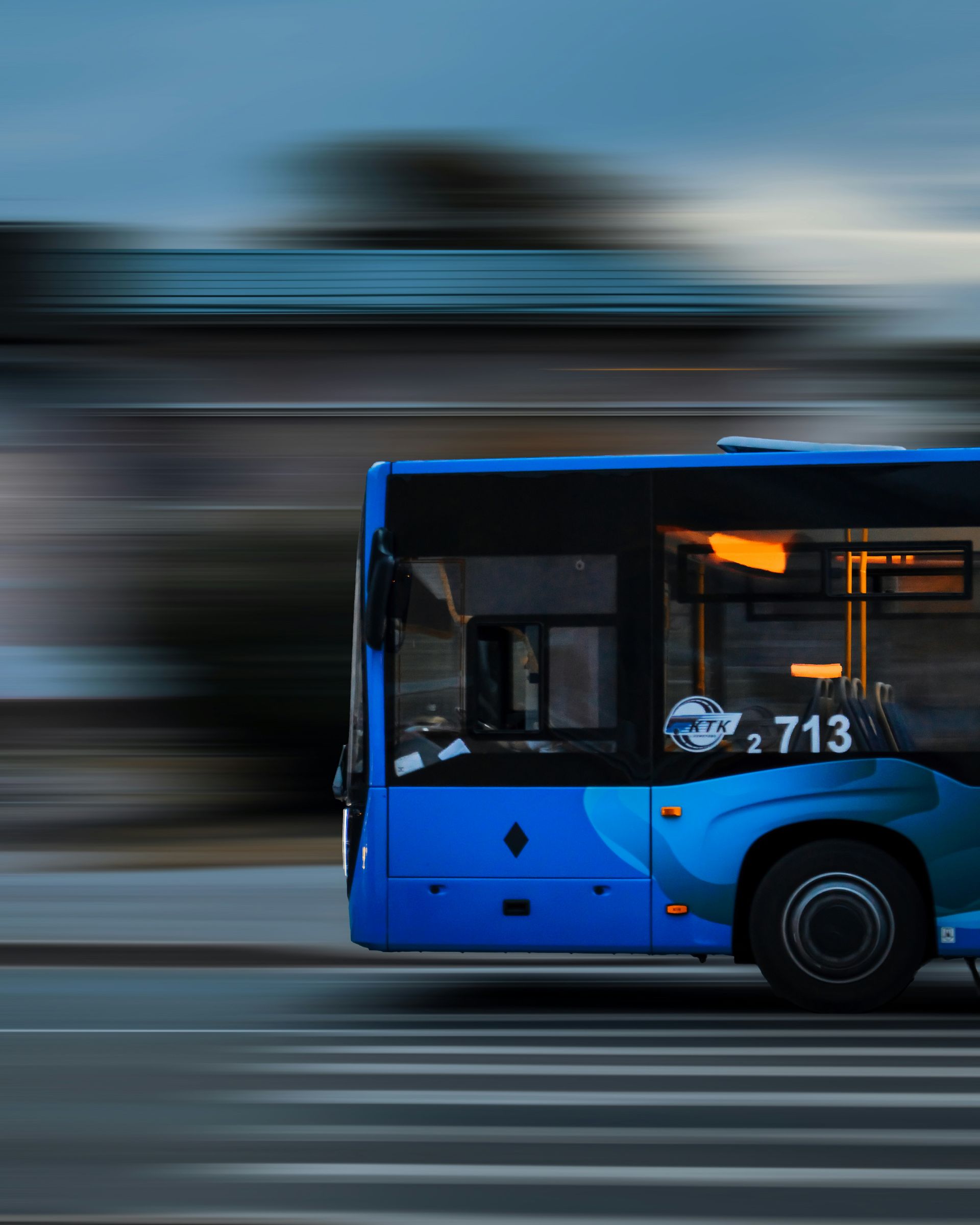 Blue bus in motion, driving on a road. Daytime with motion blur.