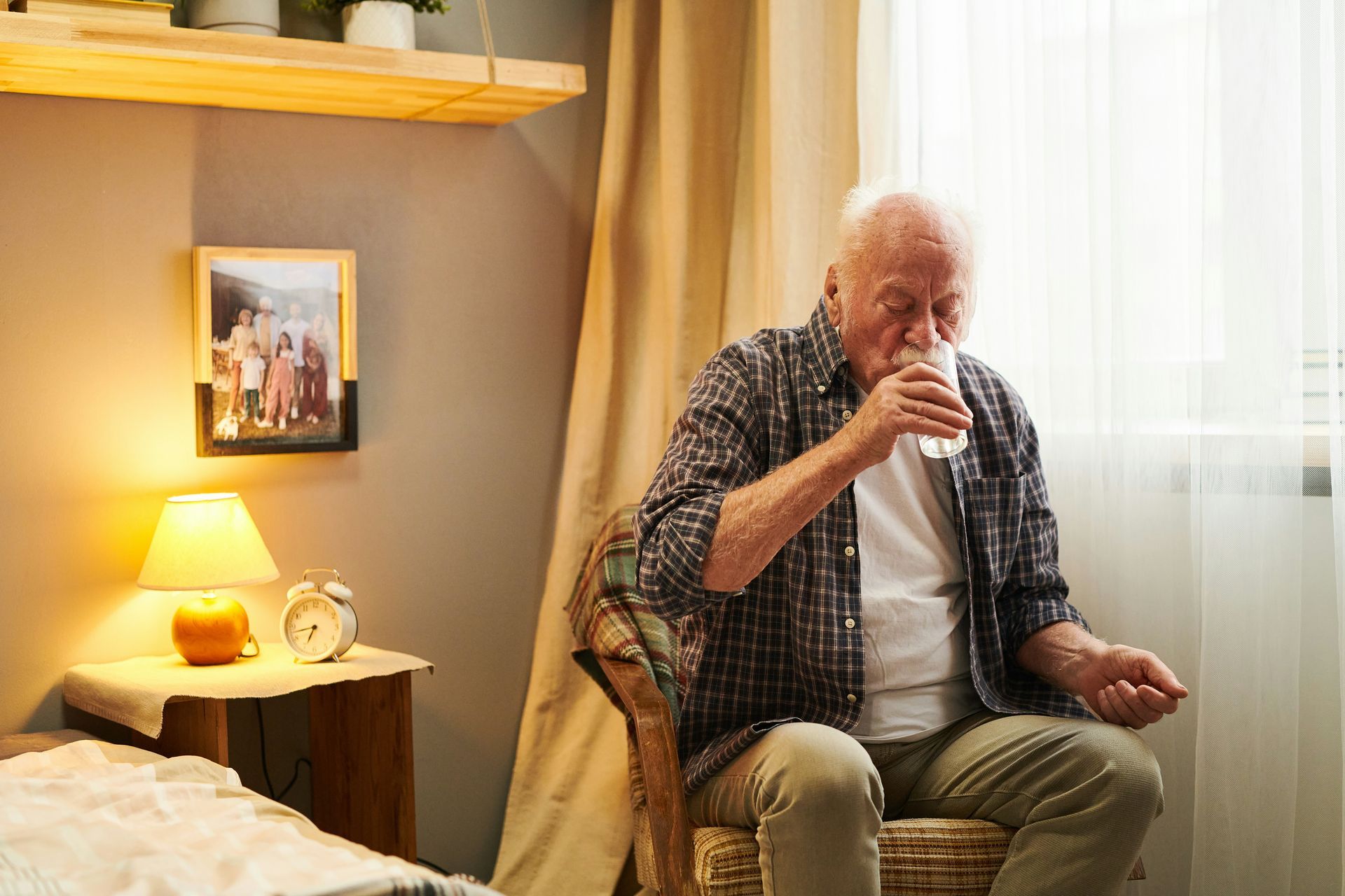 Older person taking medication with water in a bedroom.