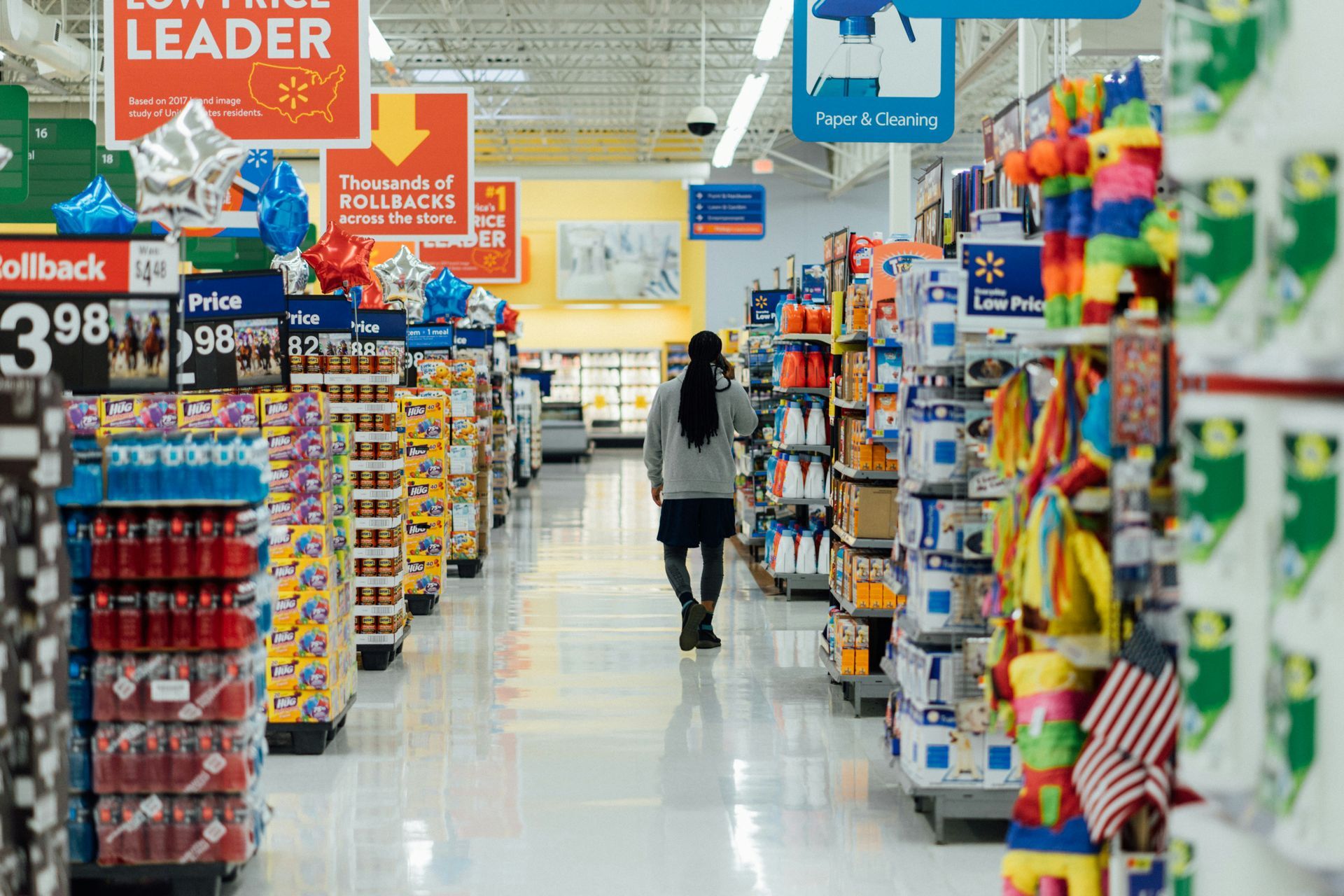 Person walking down an aisle in a Walmart store, surrounded by shelves of merchandise.