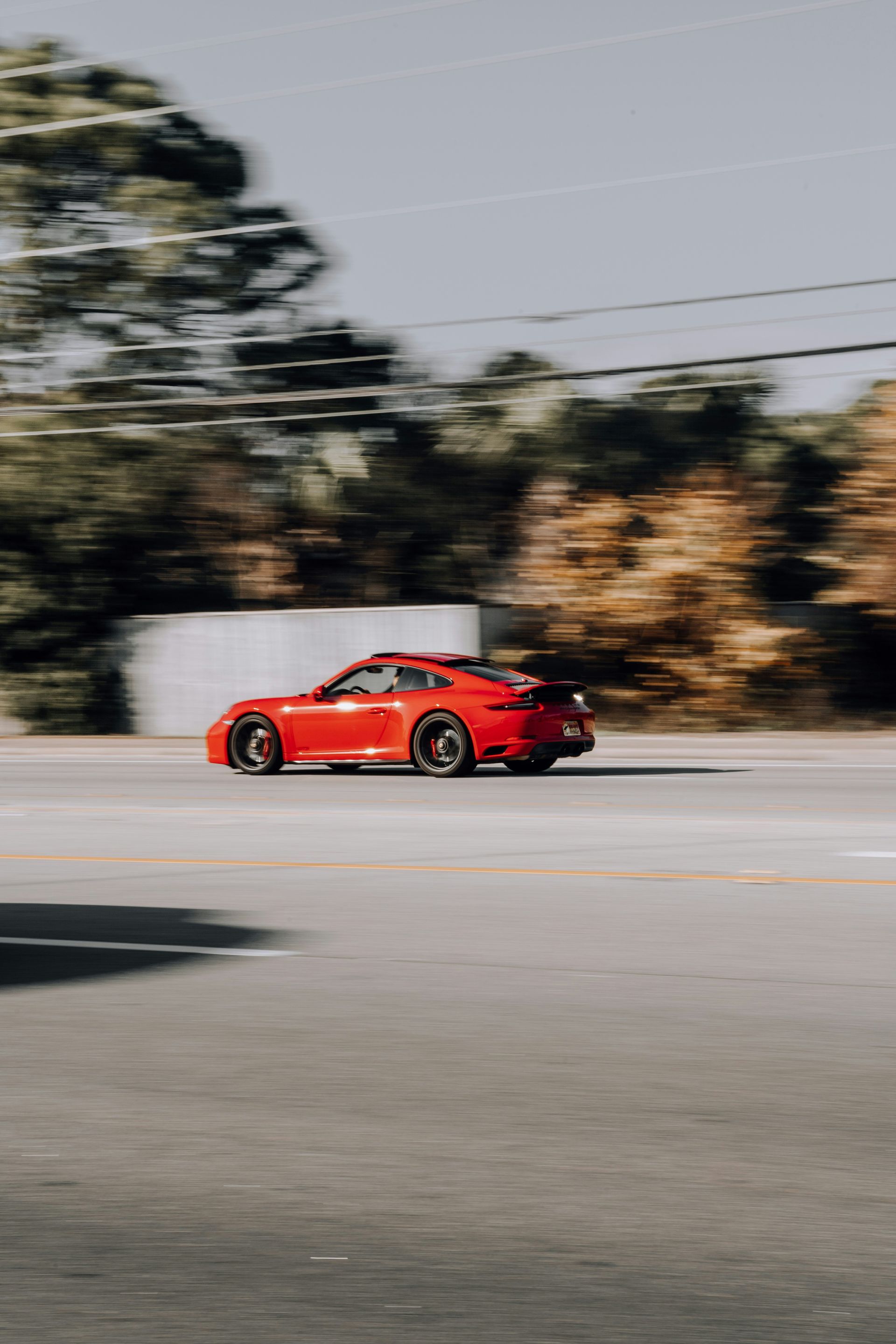 Red sports car speeding on a road with blurred background of trees and a building.
