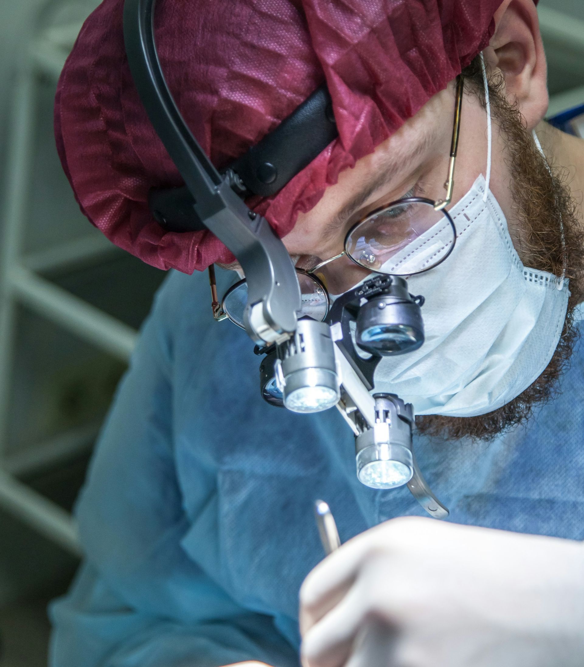 Surgeon wearing headlamp and loupes, operating room, medical procedure.