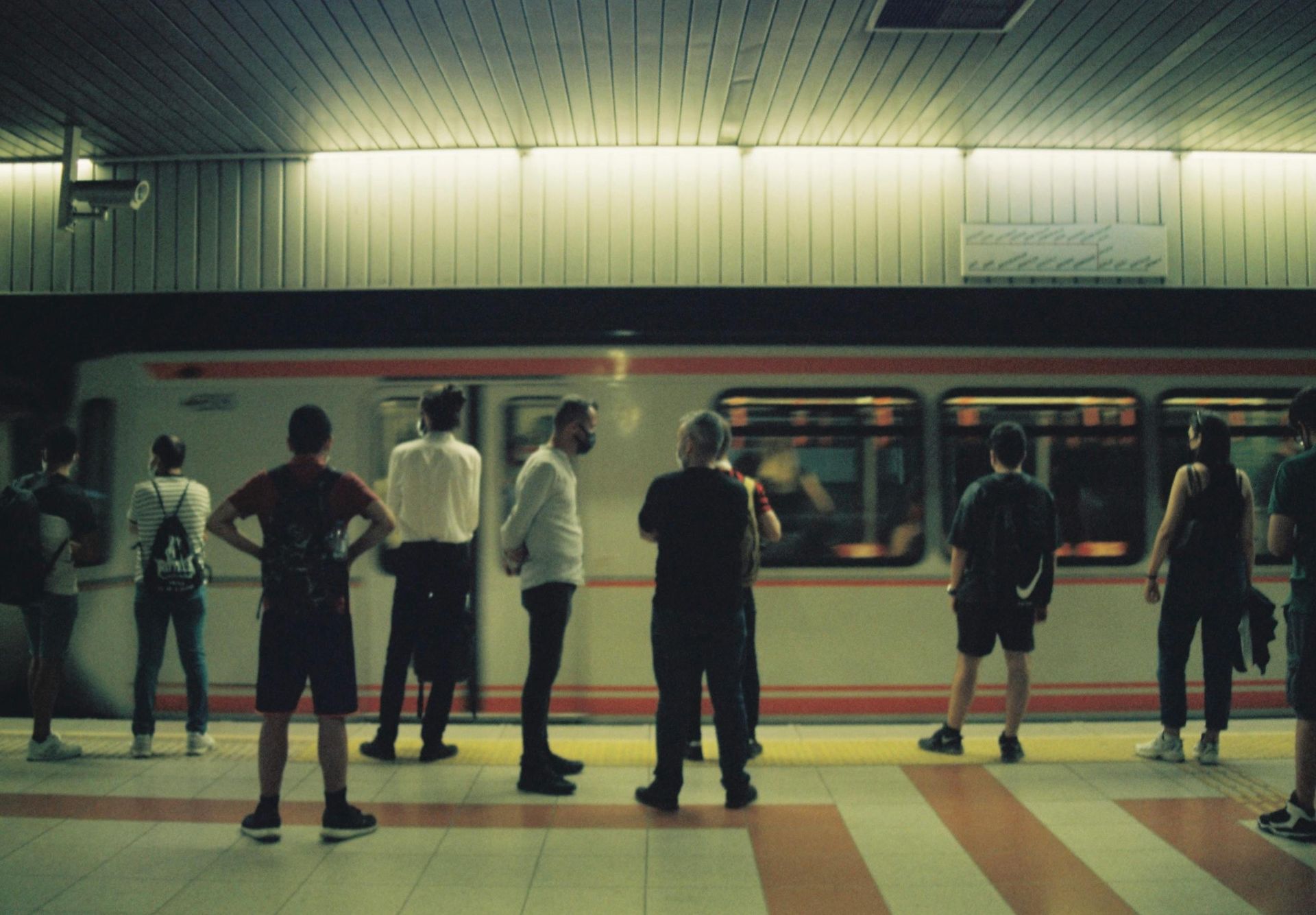 People waiting for a train at a subway station. Subway car with orange stripe visible.