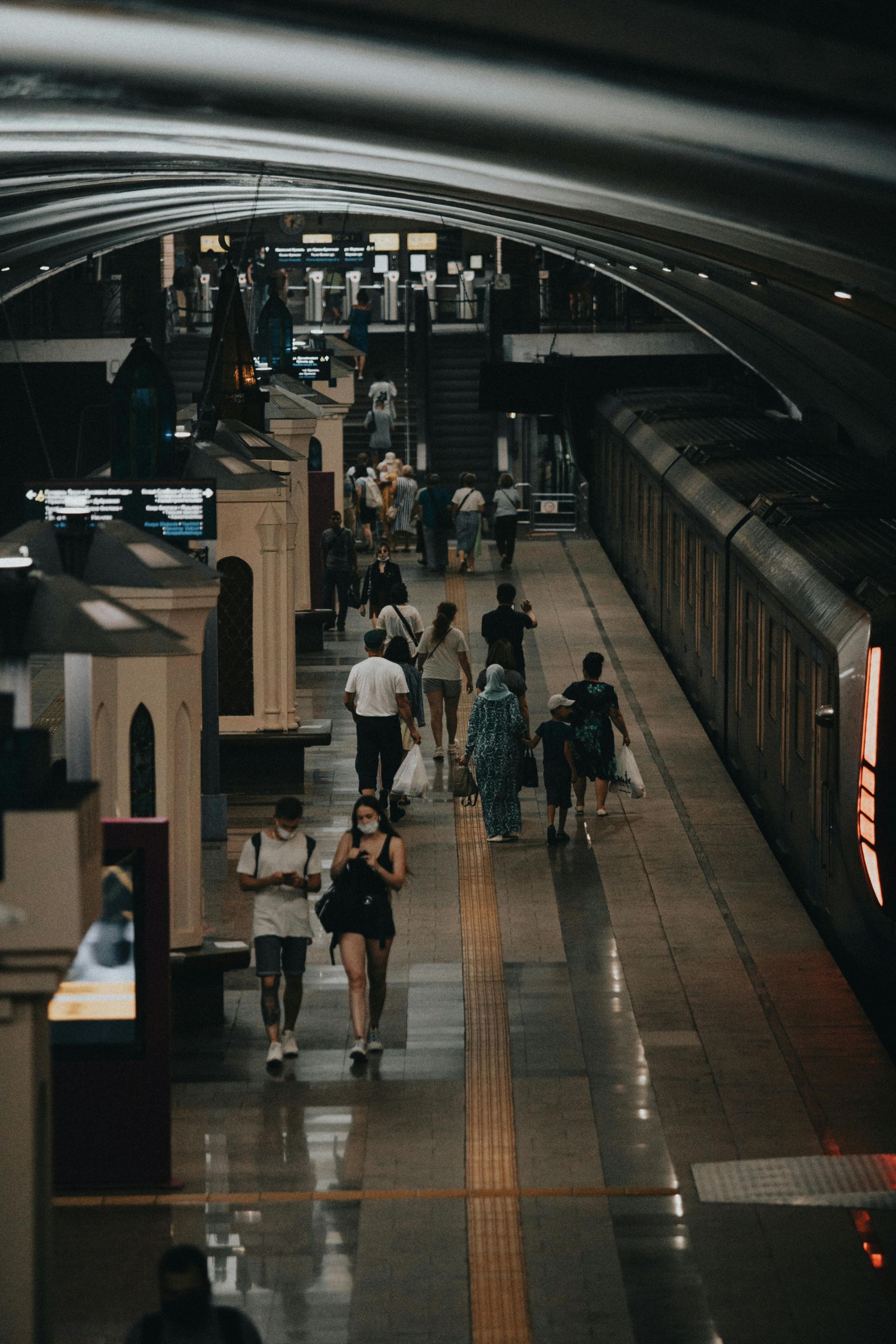 People walking on a subway platform next to a train. Dimly lit, with a curved ceiling.