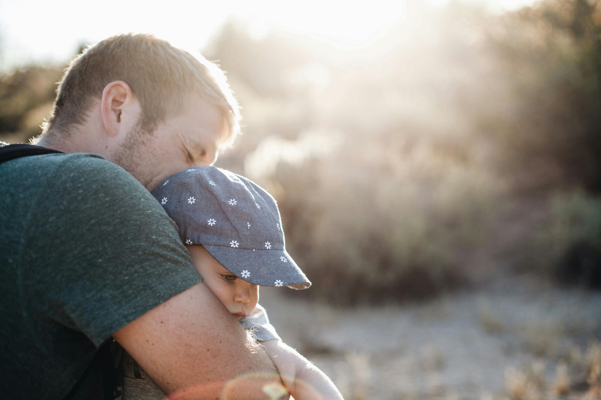 Father embracing child, warm sunlight in outdoor setting.