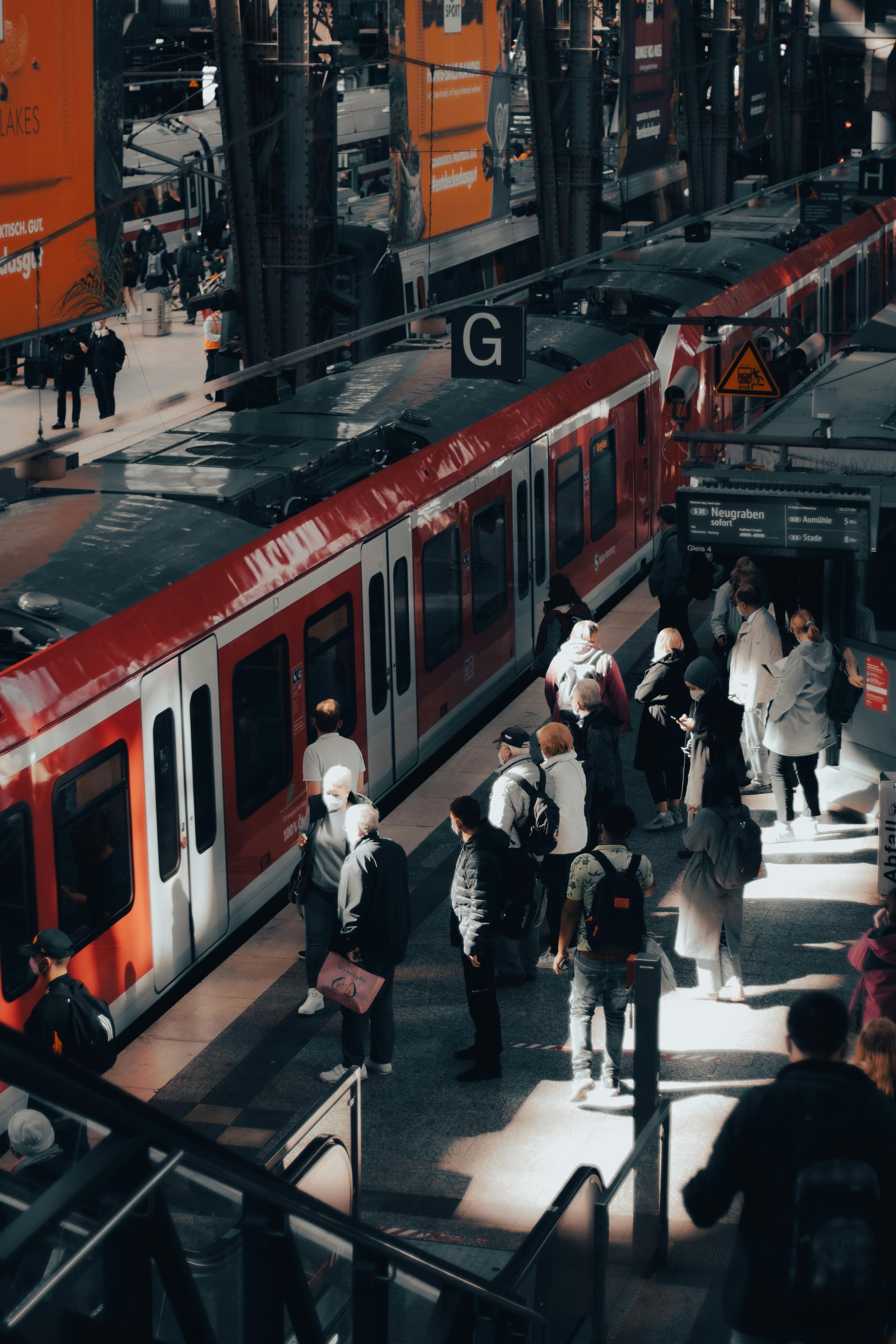 Red and white train at a crowded station platform; people boarding and waiting.