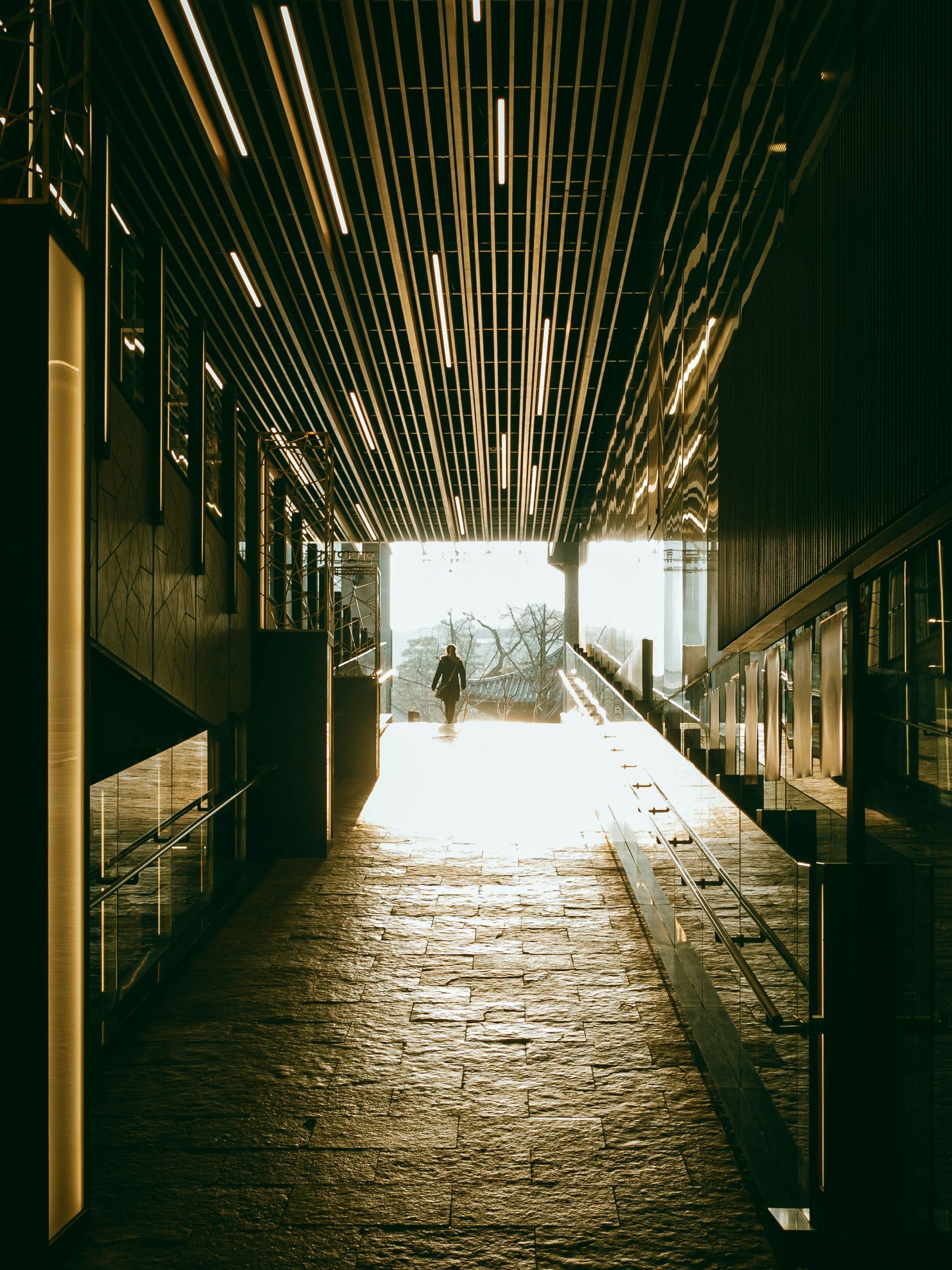 Long, dark corridor with bright exit; a person walks toward the light.