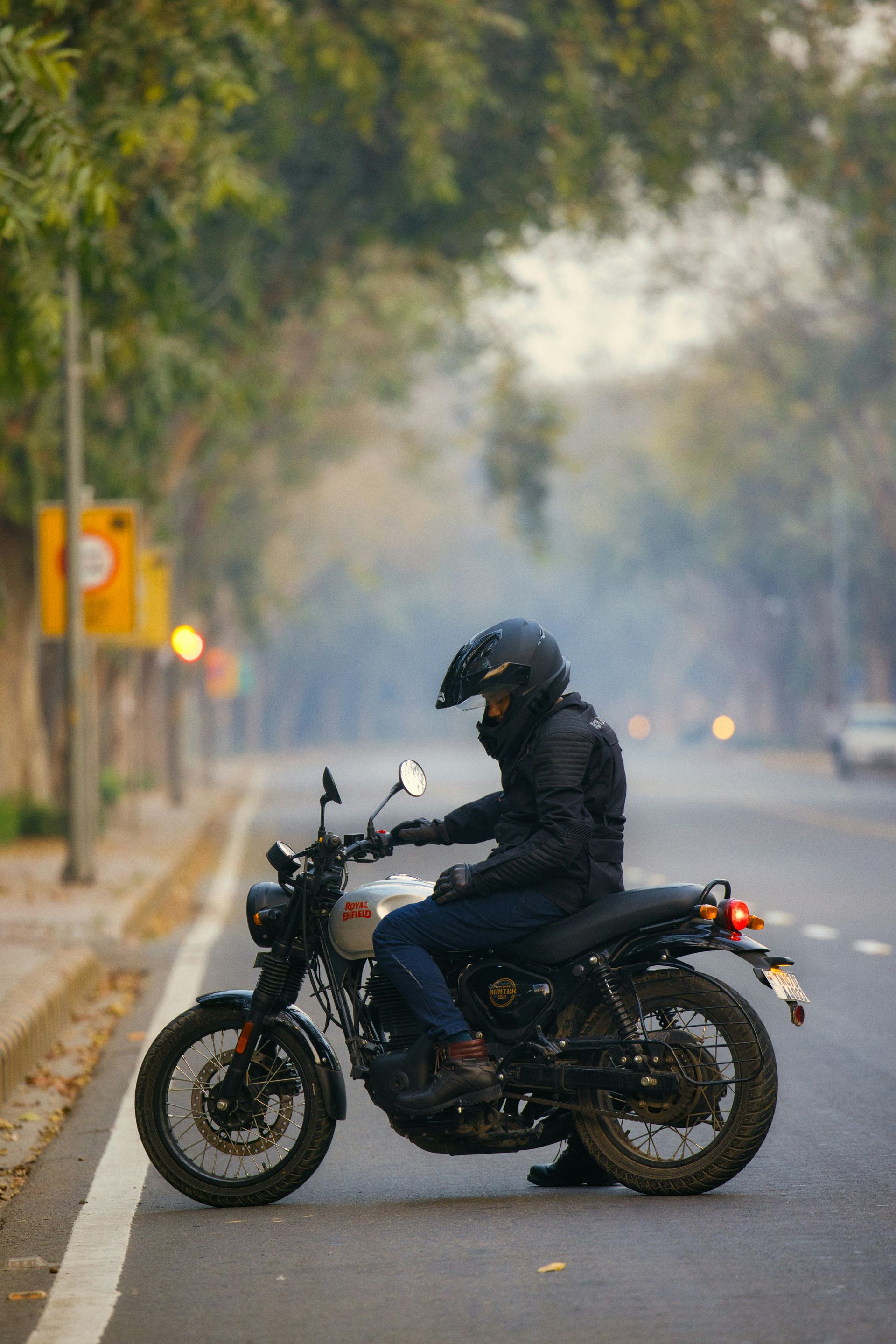 Motorcyclist on a black motorcycle, on a road lined with trees. Foggy atmosphere.