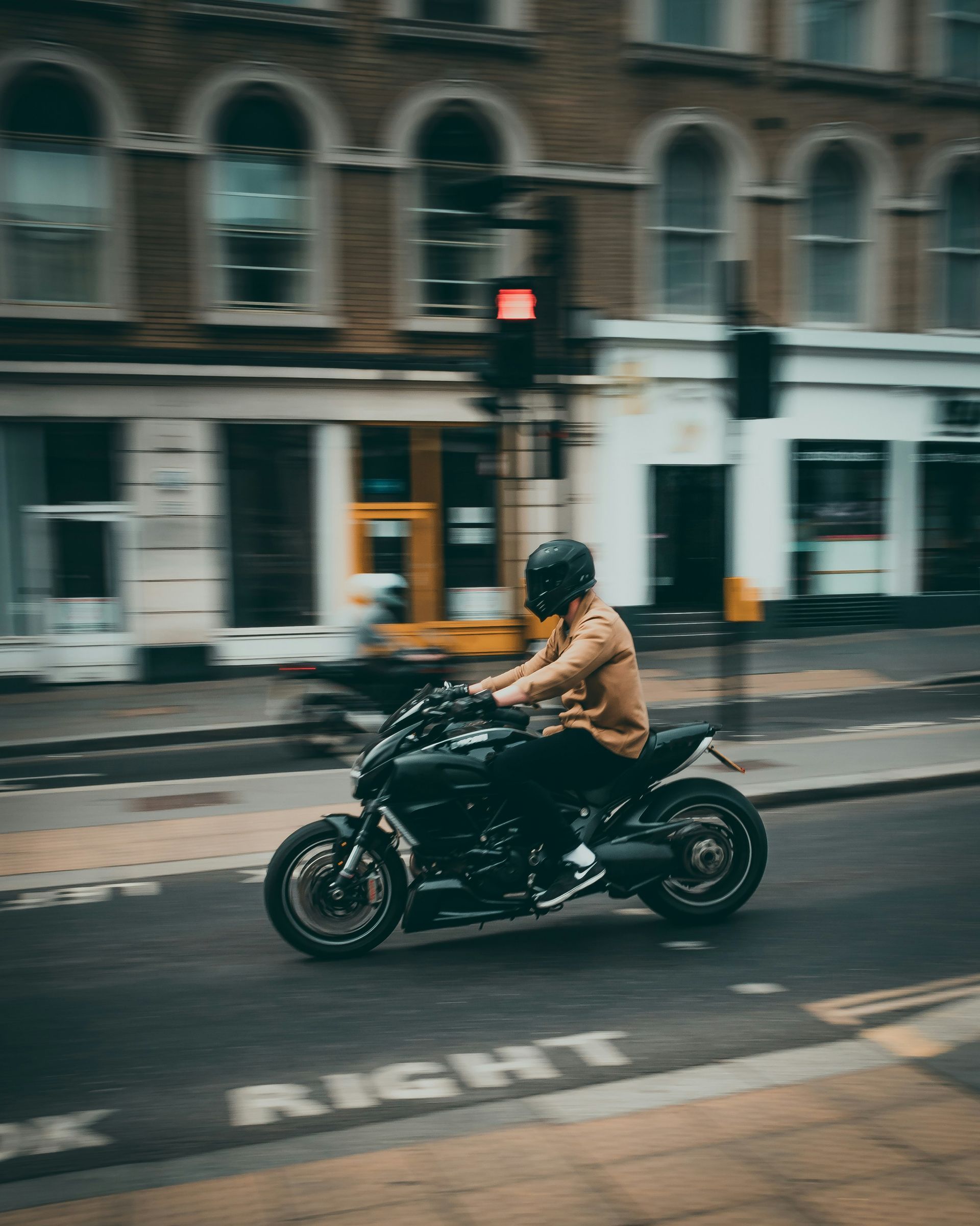 Motorcyclist on black bike speeding down street with blurred buildings.