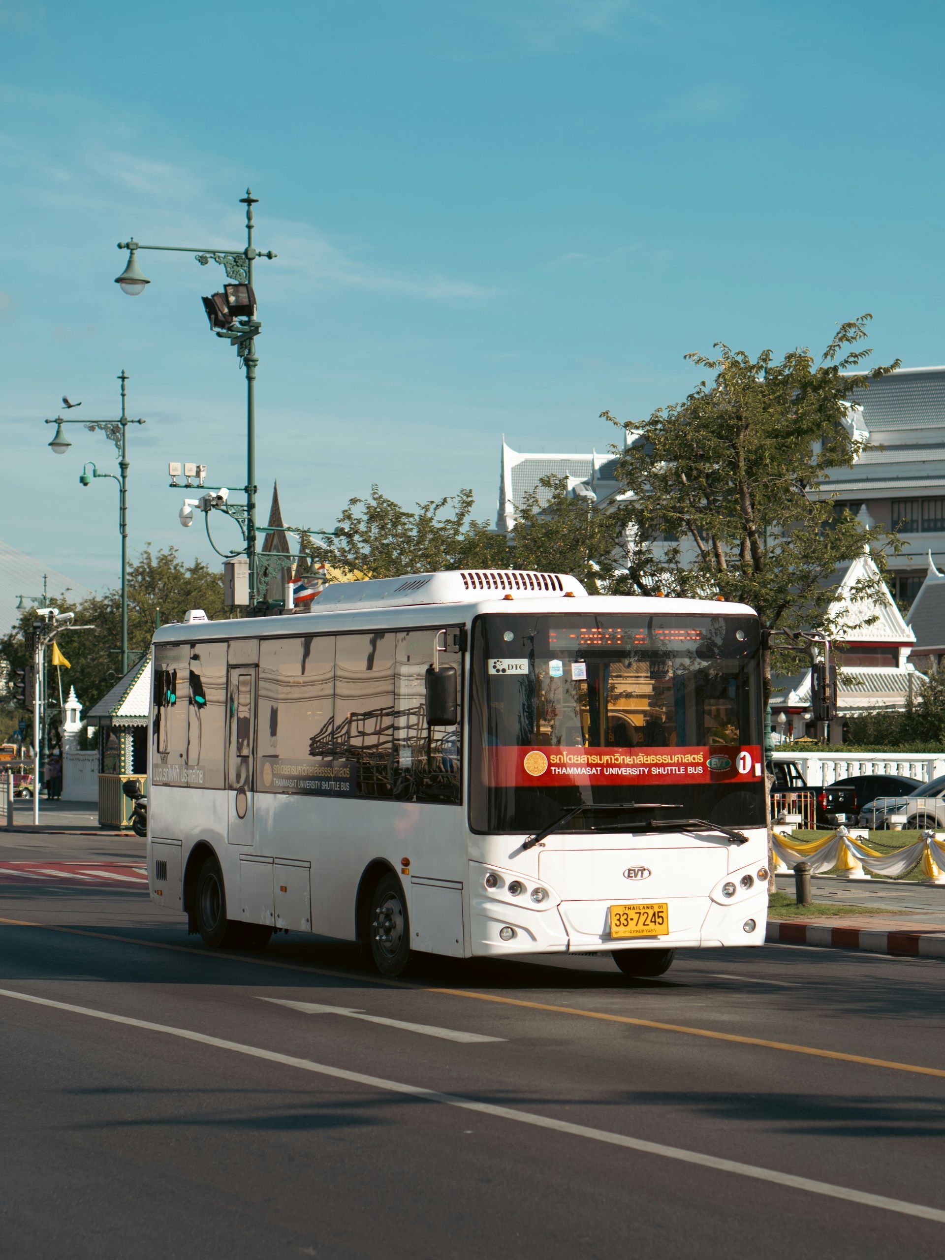 White bus driving on a city road with a blue sky background.