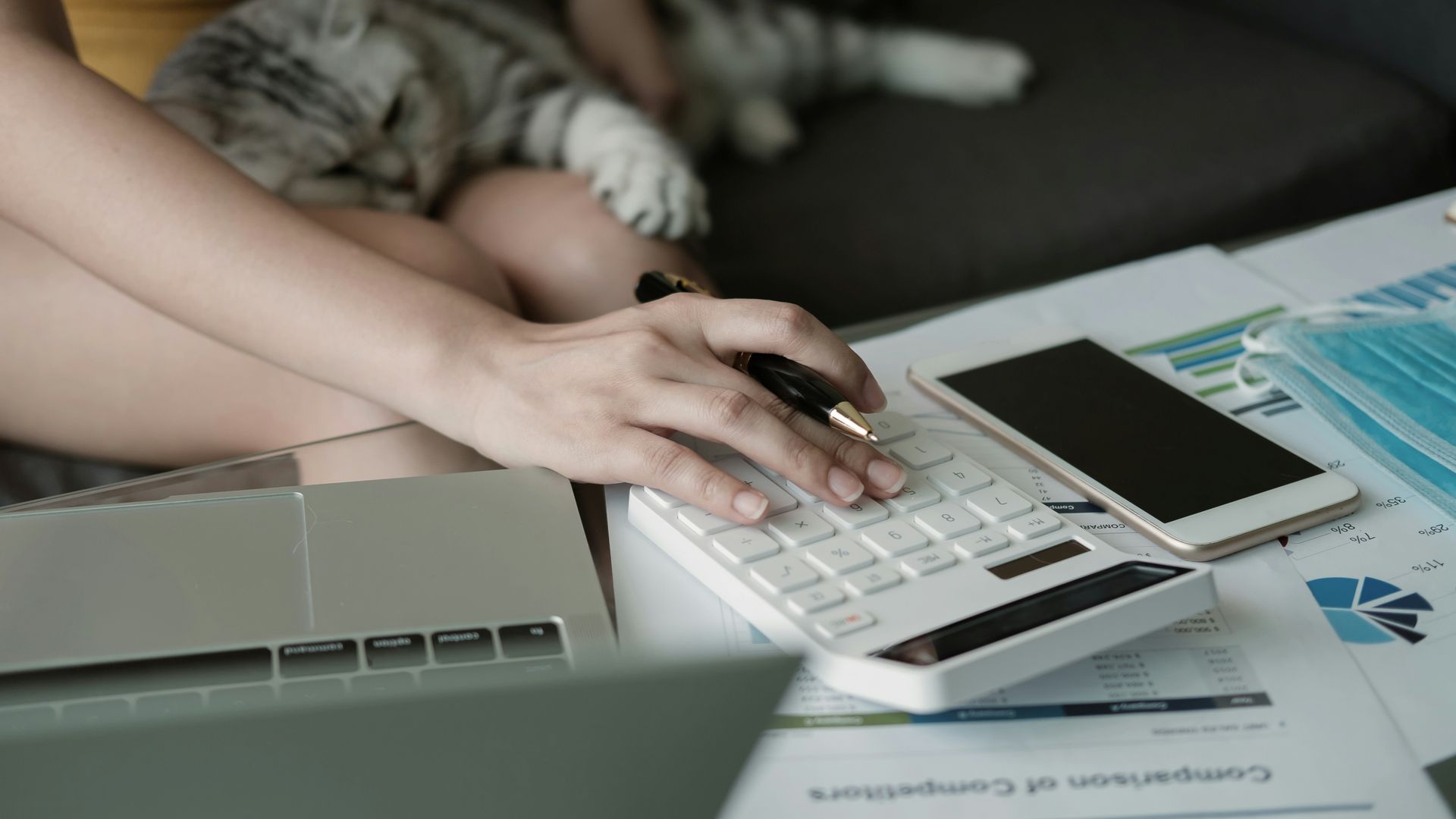 Person in a white shirt using a calculator at a wooden desk, writing and reviewing financial data.