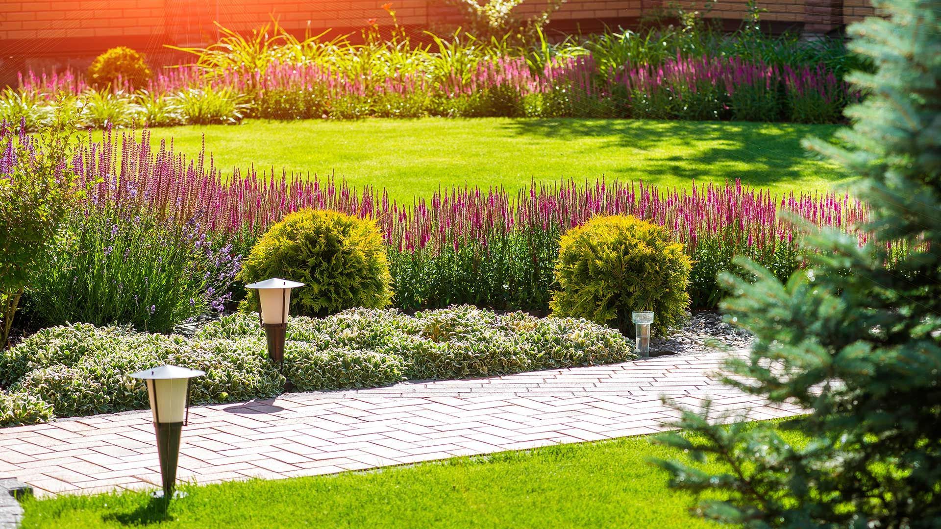 A lush green garden with a brick walkway and flowers.