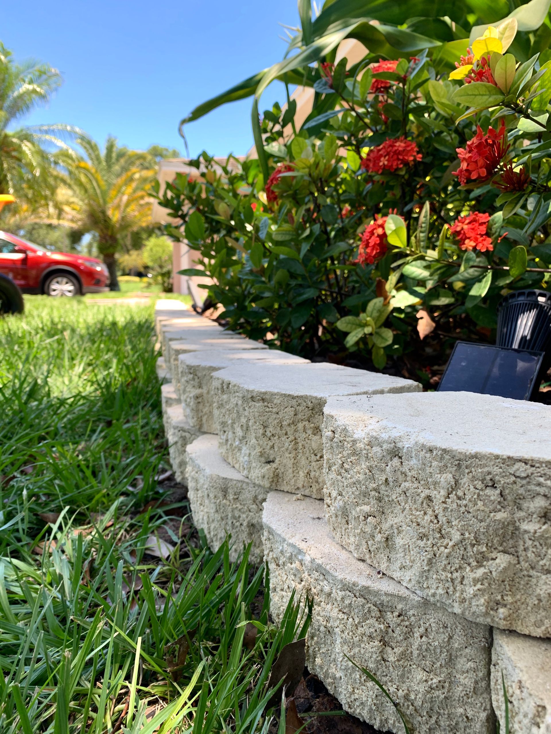 A stone wall surrounds a garden with flowers and a car parked in the background.