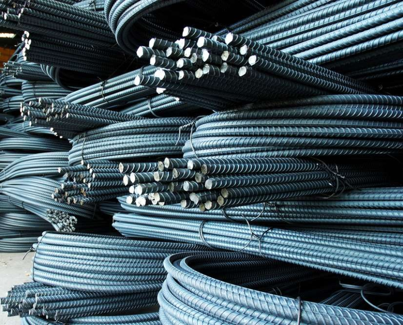 Pile di fasci di barre d'acciaio per cemento armato disposte orizzontalmente, che mostrano le barre grigie nervate con le estremità tagliate.