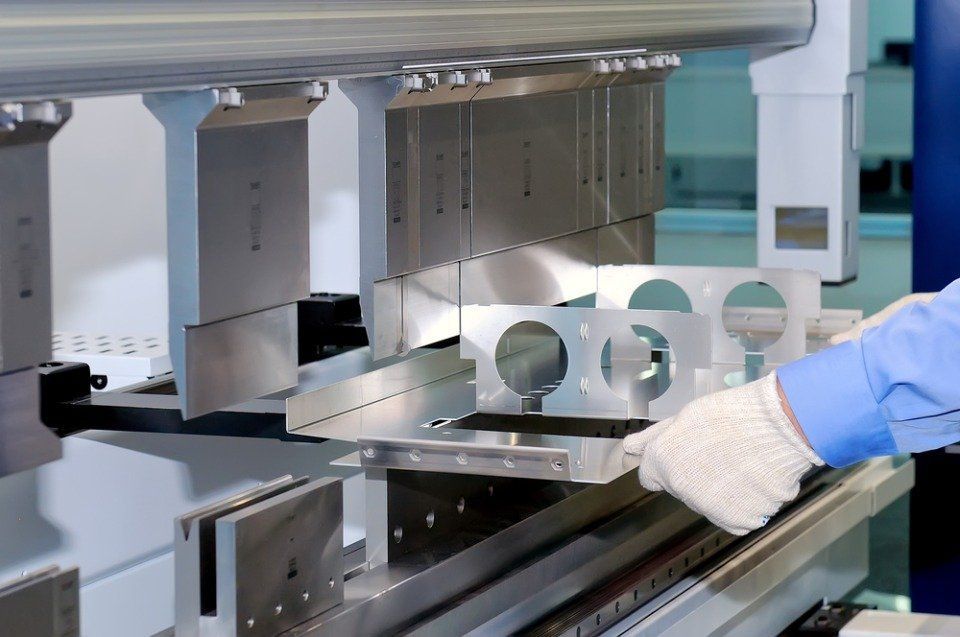 Mano guantata che aziona un macchinario industriale per la lavorazione dei metalli in un ambiente di produzione pulito.