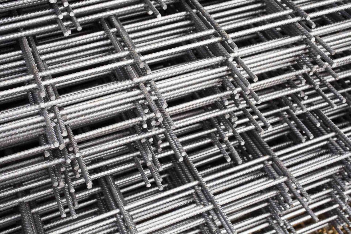 Pile di barre o tondini di metallo argentato, raggruppati secondo uno schema industriale incrociato.