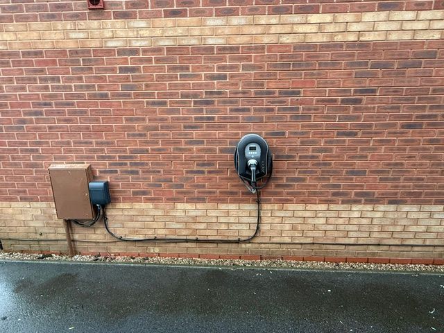 Two outdoor charging units mounted on a brick wall beside a wet pavement.