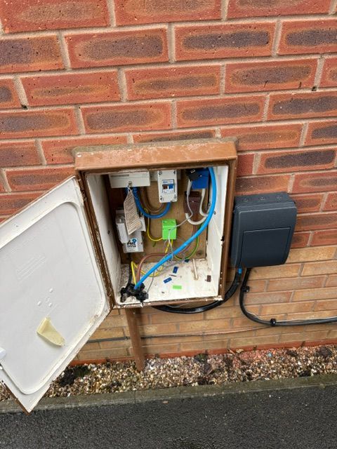 Open outdoor utility box on brick wall with exposed wiring and meter components.
